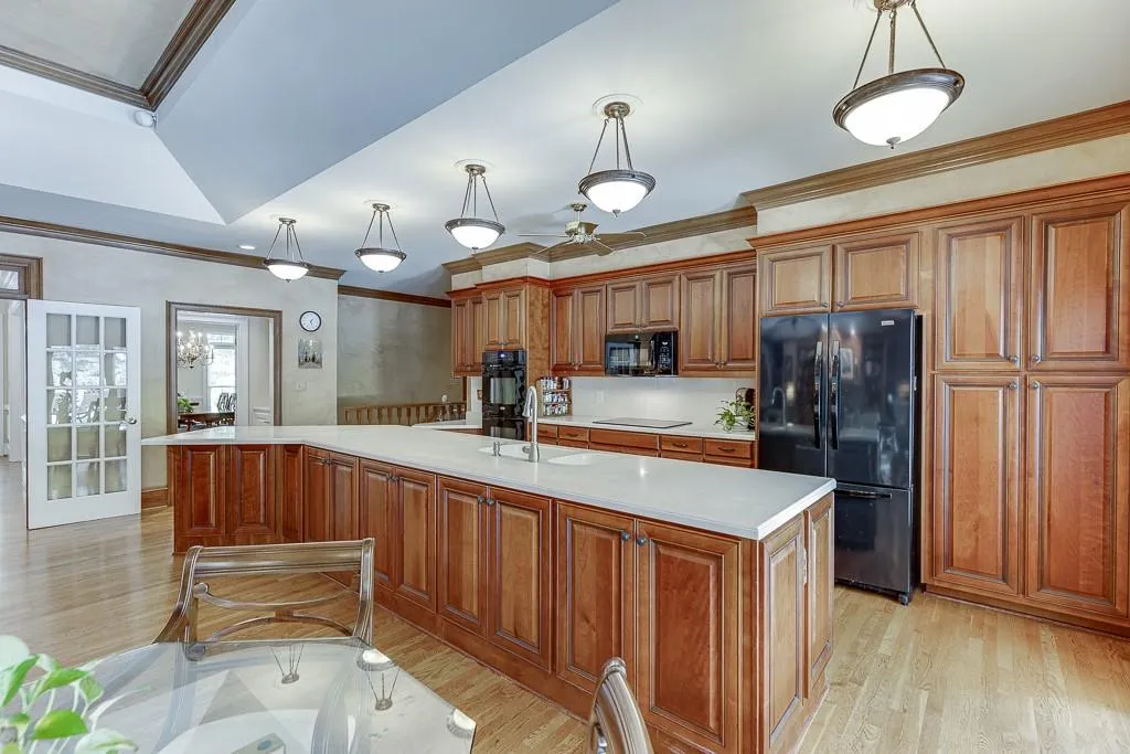 Kitchen with an island with sink, black appliances, hanging light fixtures, and ornamental molding