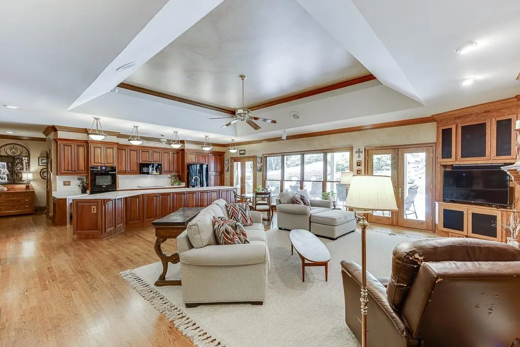 Living room featuring light wood-type flooring, a raised ceiling, ornamental molding, and ceiling fan
