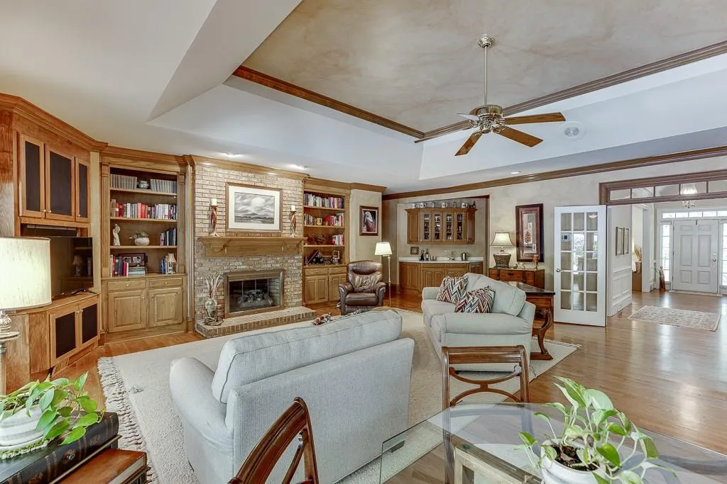 Living room with ceiling fan, built in features, a tray ceiling, a fireplace, and light hardwood / wood-style floors