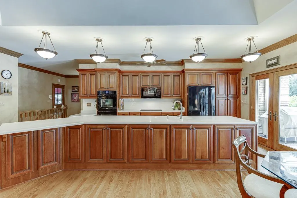 Kitchen with light wood-type flooring, sink, black appliances, decorative light fixtures, and ornamental molding