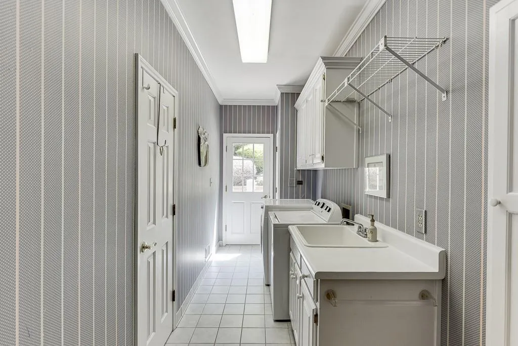 Washroom featuring cabinets, light tile patterned flooring, sink, crown molding, and washing machine and dryer