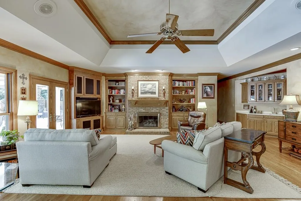 Living room with ceiling fan, a tray ceiling, a fireplace, and light hardwood / wood-style floors