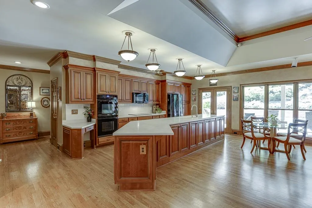 Kitchen featuring a large island with sink, black appliances, light hardwood / wood-style flooring, decorative light fixtures, and ornamental molding