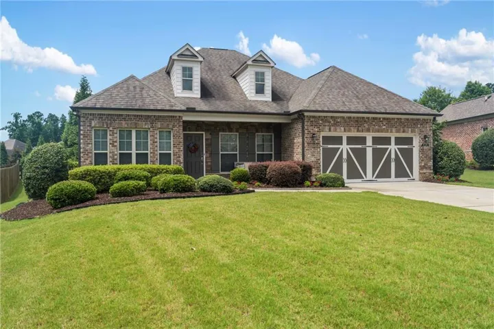 Brick and stone facade residence featuring a double-bay garage with decorative doors, architectural shingle roof, and two dormer windows