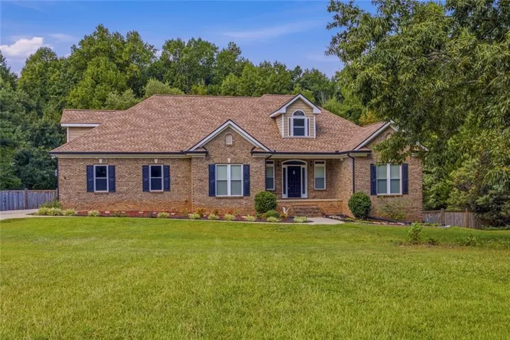 Brick exterior residence with a brown shingle roof, dark shutters, and a dormer window