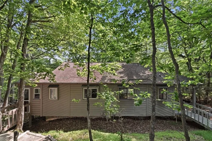 Wooded setting with mature trees, neutral-toned siding, and multiple windows