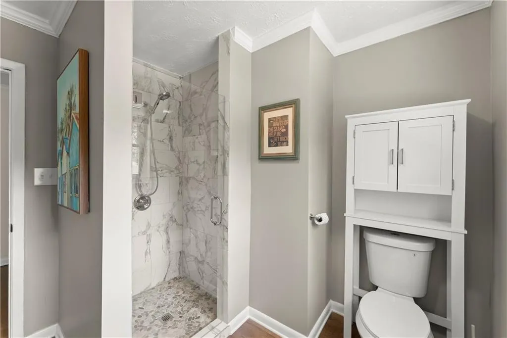 Bathroom featuring a marble finish shower, crown molding, a textured ceiling, and wood finished floors
