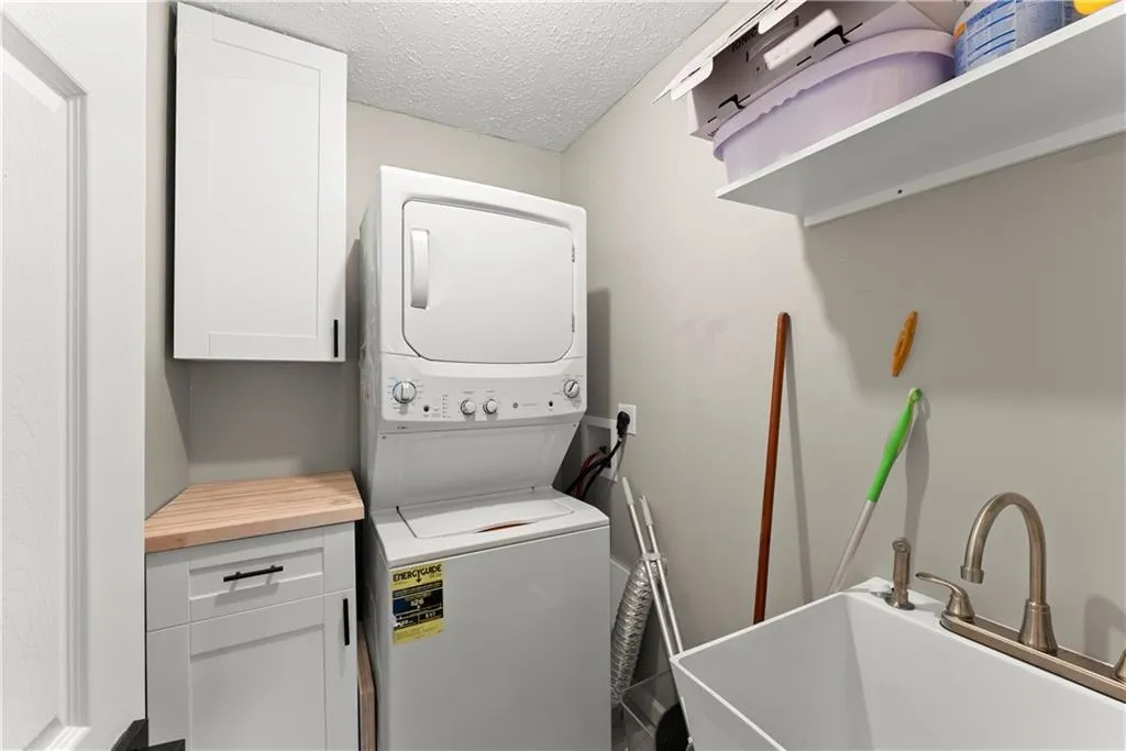 Washroom with a textured ceiling, stacked washer and clothes dryer, and cabinet space