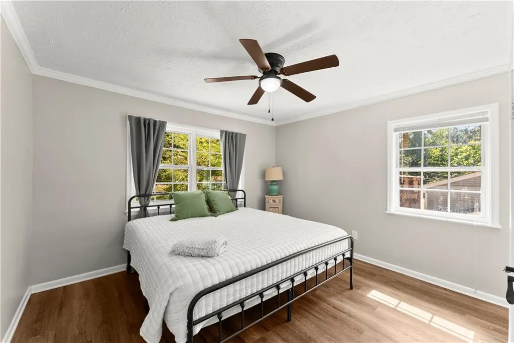 Bedroom with wood finished floors, ornamental molding, multiple windows, a textured ceiling, and ceiling fan