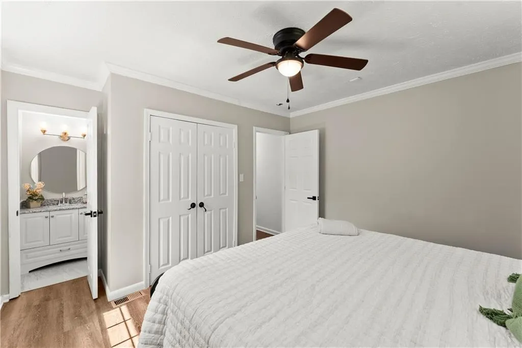 Bedroom featuring crown molding, light wood-type flooring, a ceiling fan, a closet, and ensuite bathroom