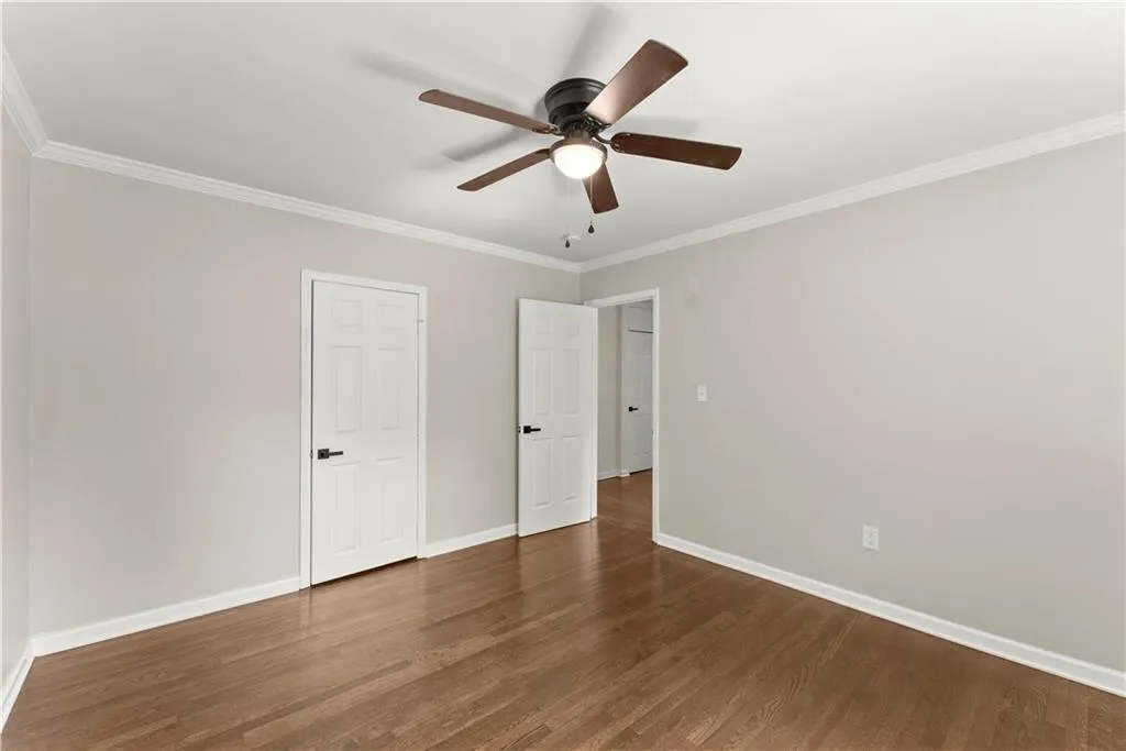 Unfurnished bedroom featuring crown molding, dark wood-style floors, and a ceiling fan