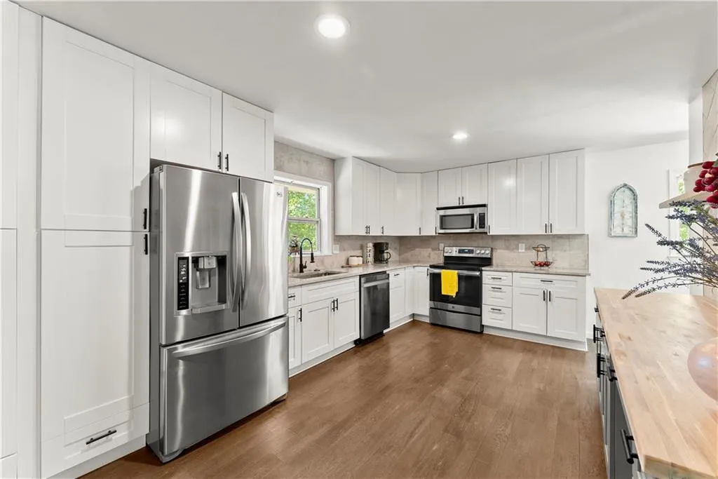 Kitchen with white cabinets, appliances with stainless steel finishes, light stone counters, dark wood-type flooring, and backsplash