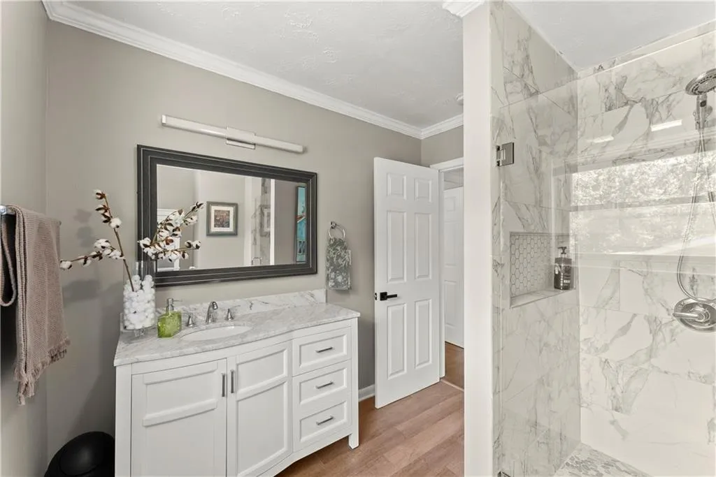 Full bath with a marble finish shower, vanity, ornamental molding, light wood-style floors, and a textured ceiling