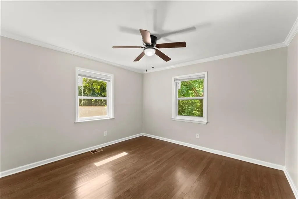 Empty room featuring ornamental molding, dark wood finished floors, plenty of natural light, and a ceiling fan