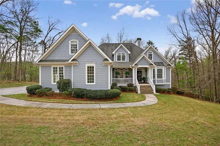 View of front of property with a chimney, a front lawn, covered porch, and roof with shingles