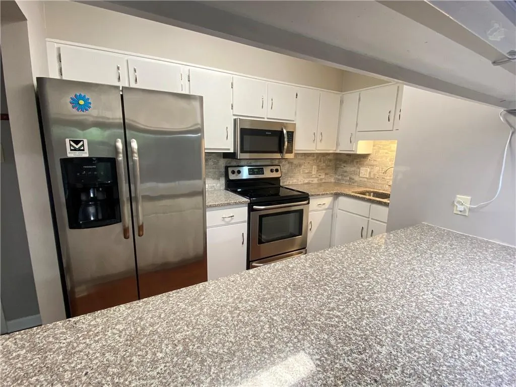 Kitchen with sink, appliances with stainless steel finishes, white cabinets, and backsplash