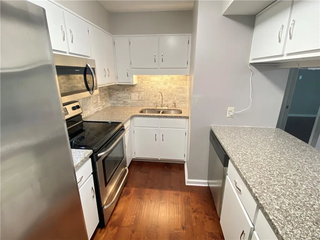Kitchen featuring appliances with stainless steel finishes, white cabinets, sink, backsplash, and dark hardwood / wood-style flooring