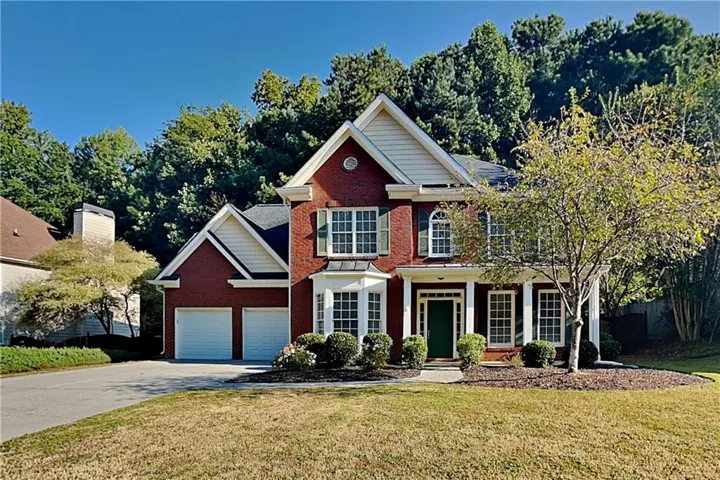 Red brick exterior with white trim, two-car garage, covered entry, and established landscaping