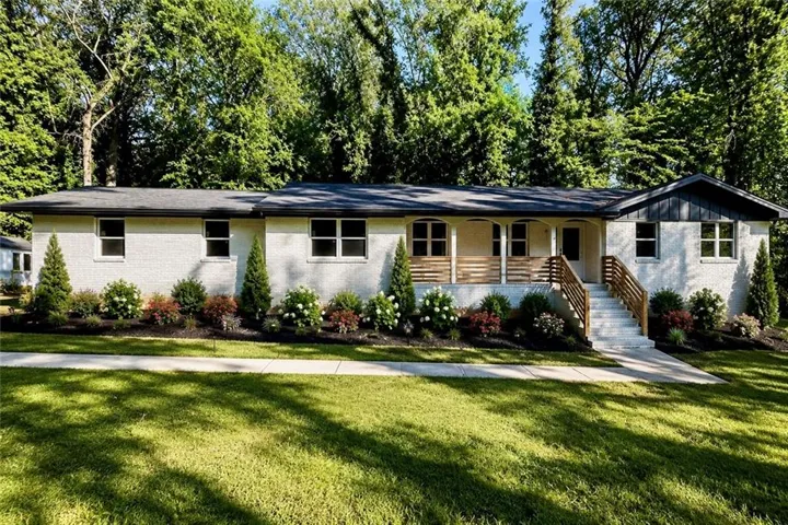 White brick exterior featuring dark trim, a covered front porch with wood slat detailing, and a tiered concrete walkway