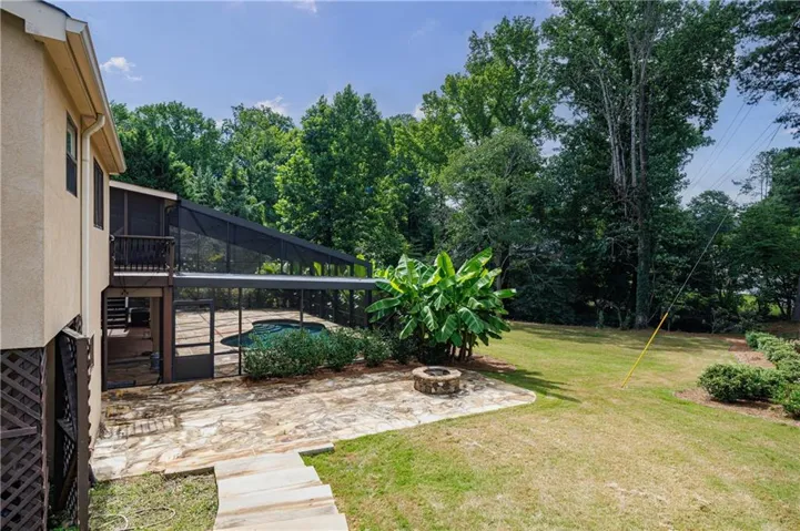 Screened pool enclosure with a flagstone patio, an elevated balcony, and a dedicated fire pit area