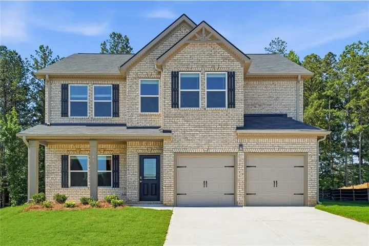 Two-story brick exterior featuring a covered front porch, dark-paneled entry door, dual garage doors, and a concrete driveway
