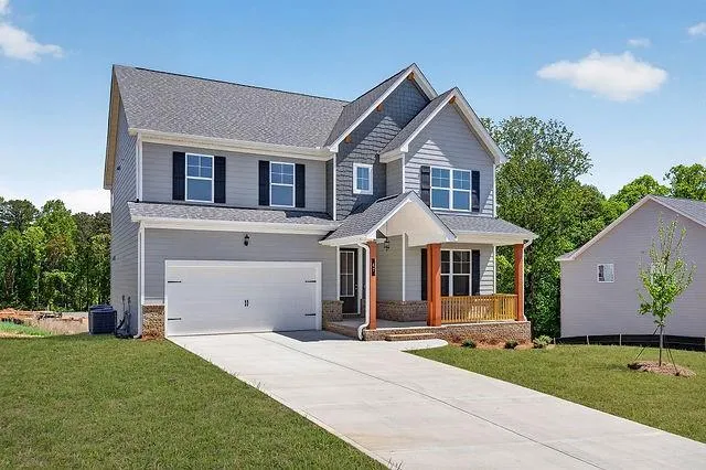 Two-story residential structure featuring a covered front porch with wood columns and railings, an attached garage, and a concrete driveway