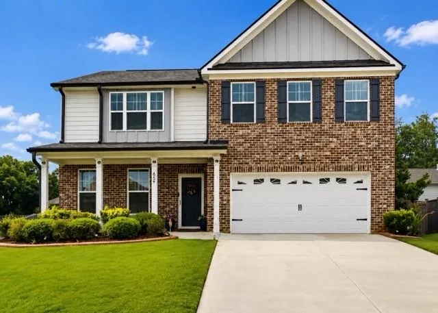 Two-story residence featuring brick and siding facade, a covered front porch with white columns, attached two-car garage, and established front landscaping