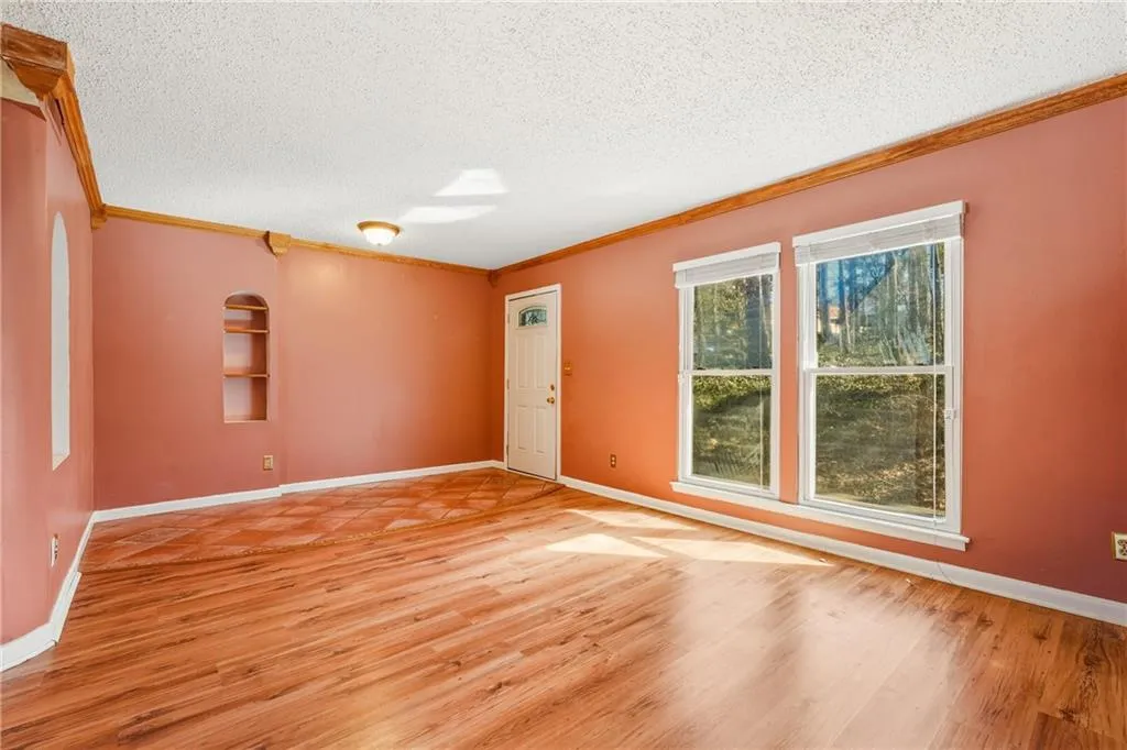 Empty room with light wood finished floors, a textured ceiling, crown molding, and built in shelves