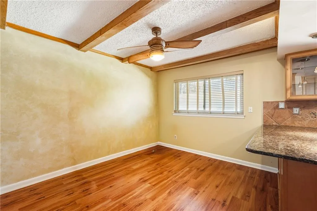 Unfurnished dining area featuring a ceiling fan, beamed ceiling, light wood-style floors, and a textured ceiling