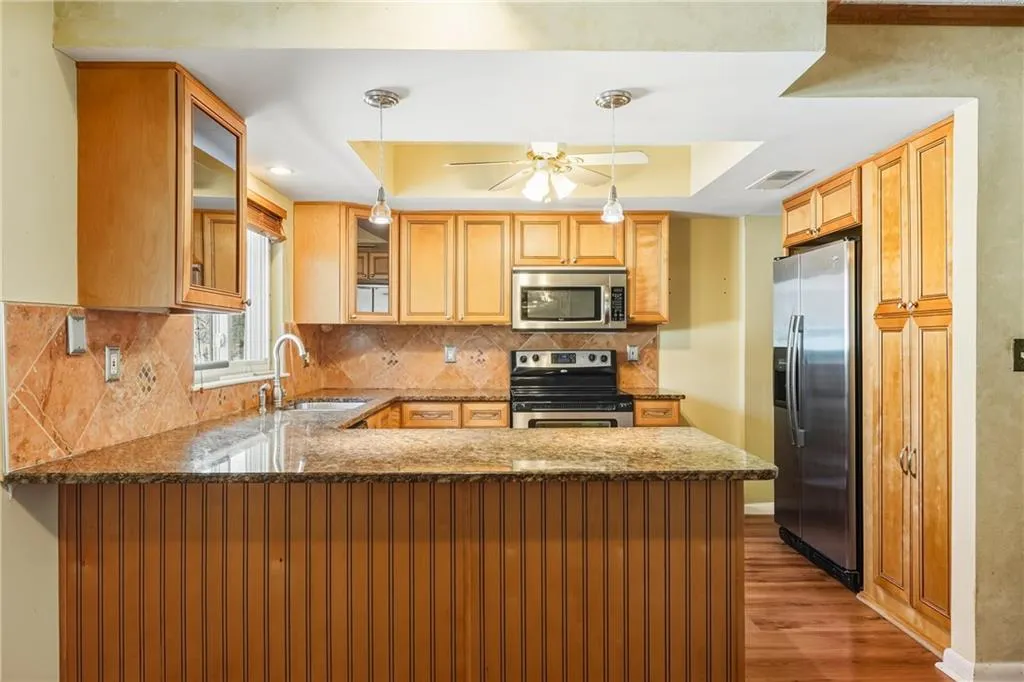 Kitchen featuring dark stone counters, a peninsula, pendant lighting, stainless steel appliances, and glass fronted cabinets