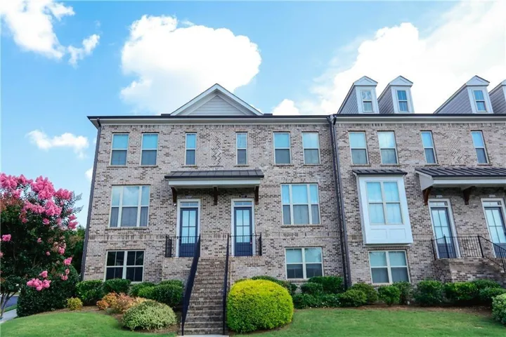 Brick-front townhome featuring multiple windows, dormer accents, and a covered entry with steps