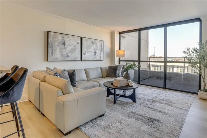 Light wood-finish flooring, full-height windows, crown molding, and an open layout define this living area