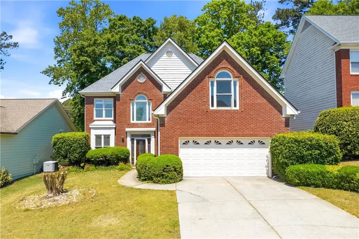 Two-story brick facade residence featuring white gabled dormers, a two-car garage with decorative transom windows, an arched entry door, and a curved concrete driveway