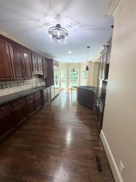 Rich wood cabinetry, wood-finish flooring, dark countertops, tile backsplash, and bay windows