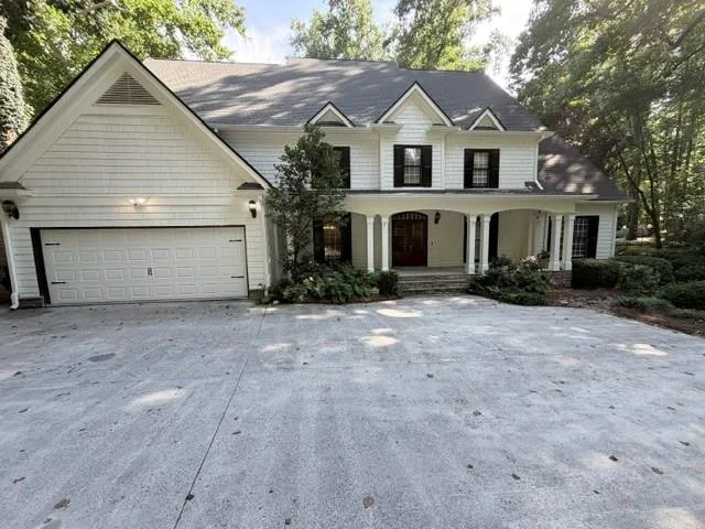Two-story residence featuring white shingle siding, a dark roof, black window shutters, a covered entry porch with white columns, and a two-car garage