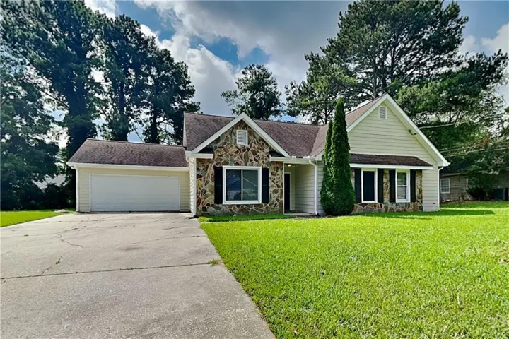 Stone facade accents, shingle roofing, attached two-car garage, manicured lawn, and mature trees