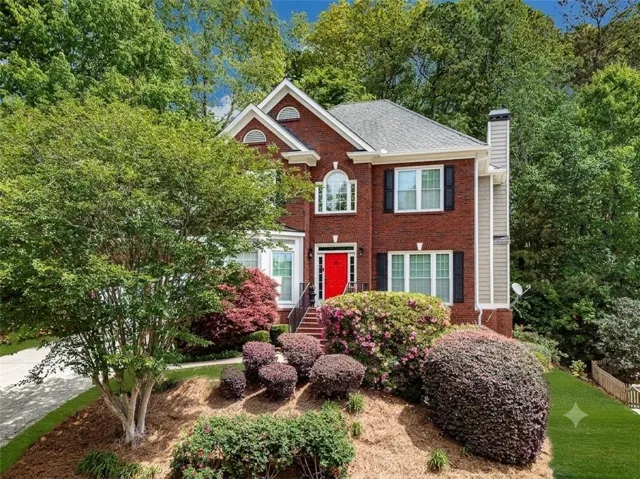 Brick facade residence featuring multiple dormer windows, a prominent red entry door, and dark window shutters