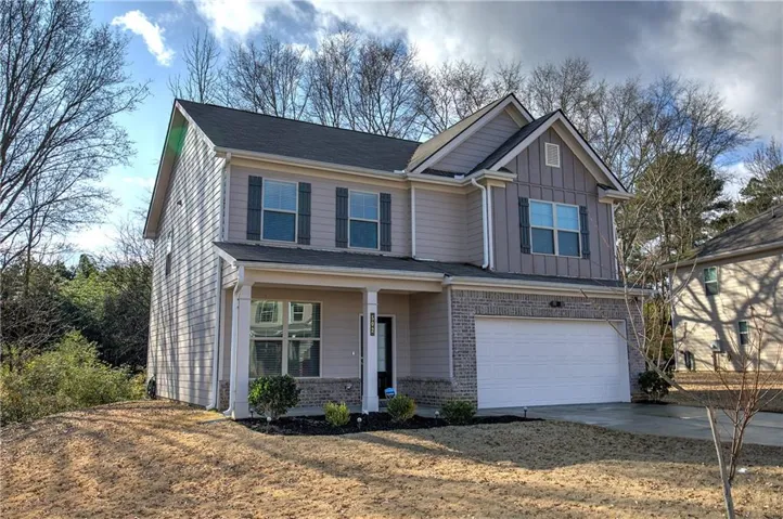 Two-story property featuring a covered front porch, an attached garage, brick veneer, gray siding, and dark window shutters