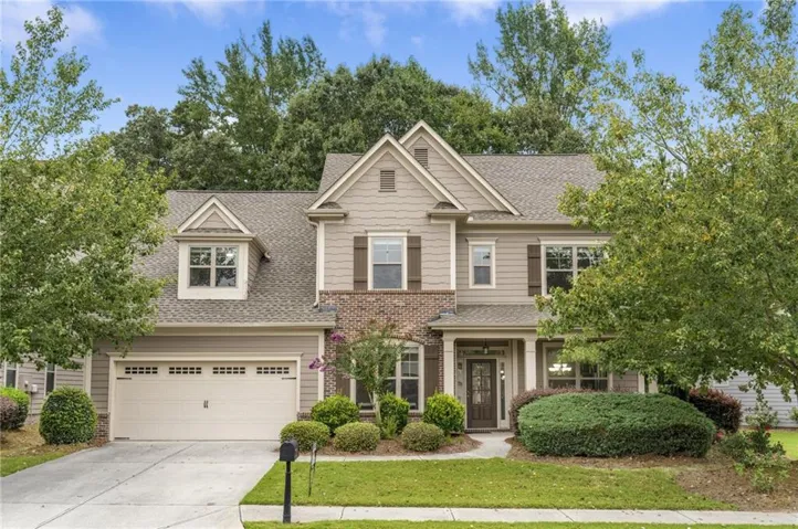 Two-story residence featuring a shingle roof, mixed material facade with brick and siding, an attached two-car garage, and a covered entry