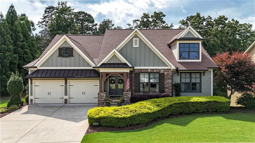 Craftsman-style residence featuring a combination of siding and stone veneer, a covered front porch with timber accents, and a two-car garage with carriage-style doors