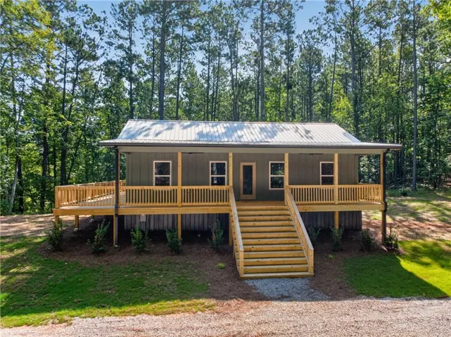 Exterior featuring a metal roof, front porch with wood railings, wood steps, and a gravel driveway