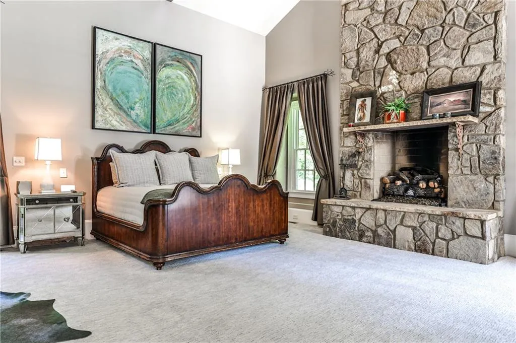 Spacious primary bedroom with stone fireplace, French doors that lead to the garden and pool area.