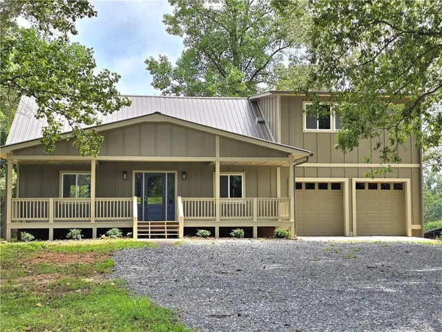 View of front of home with a porch, board and batten siding, an attached garage, driveway, and a metal roof