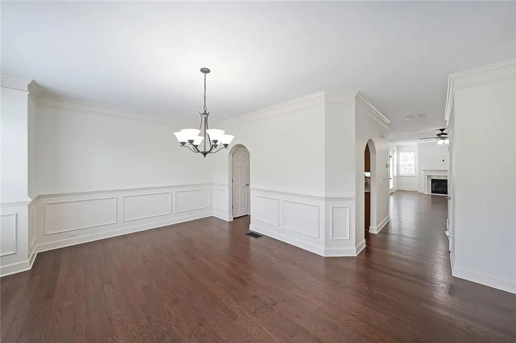 Empty room with arched walkways, a chandelier, dark wood-type flooring, a ceiling fan, and wainscoting