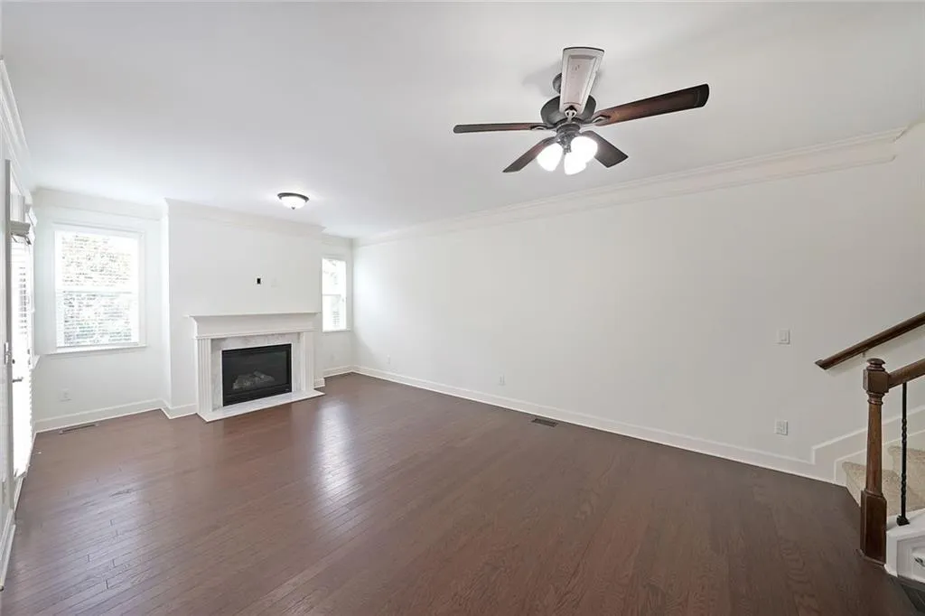 Unfurnished living room featuring crown molding, stairs, dark wood-type flooring, a high end fireplace, and a ceiling fan