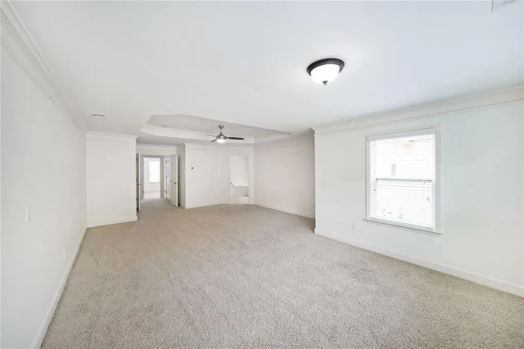 Spare room with crown molding, ceiling fan, light colored carpet, and a raised ceiling