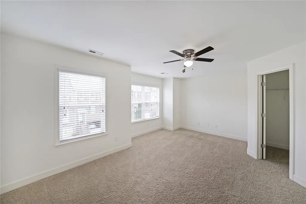 Unfurnished bedroom featuring light carpet, a ceiling fan, and a spacious closet
