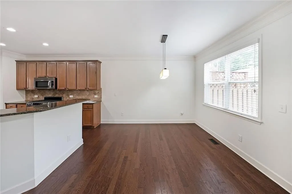 Kitchen featuring stainless steel microwave, stove, decorative backsplash, brown cabinets, and dark wood-type flooring