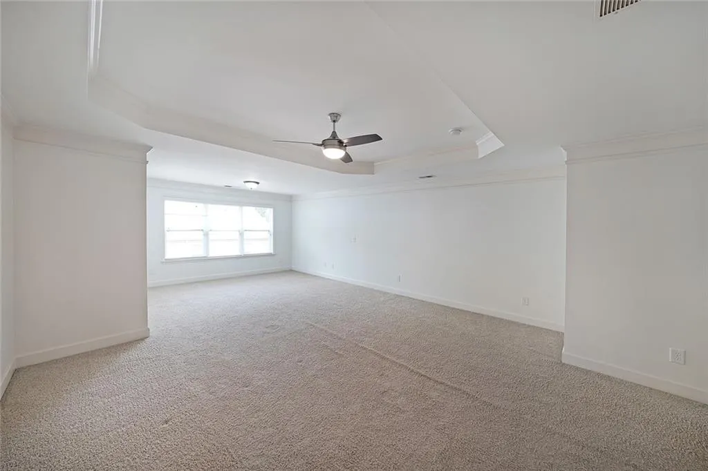 Carpeted empty room featuring a tray ceiling, crown molding, and a ceiling fan