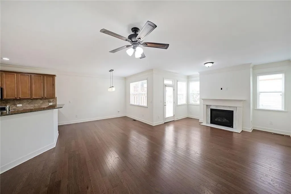 Unfurnished living room with ceiling fan, a fireplace with flush hearth, dark wood-style floors, and ornamental molding